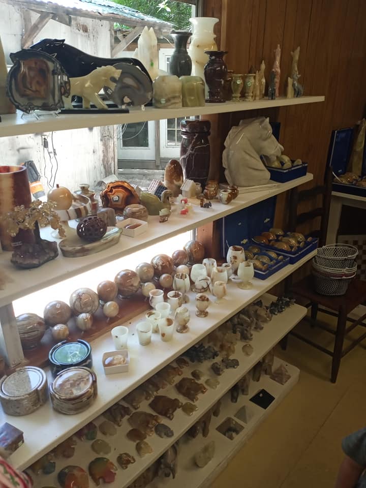 Shelves of assorted glass and ceramic crafts in a small shop, with a seated person at right