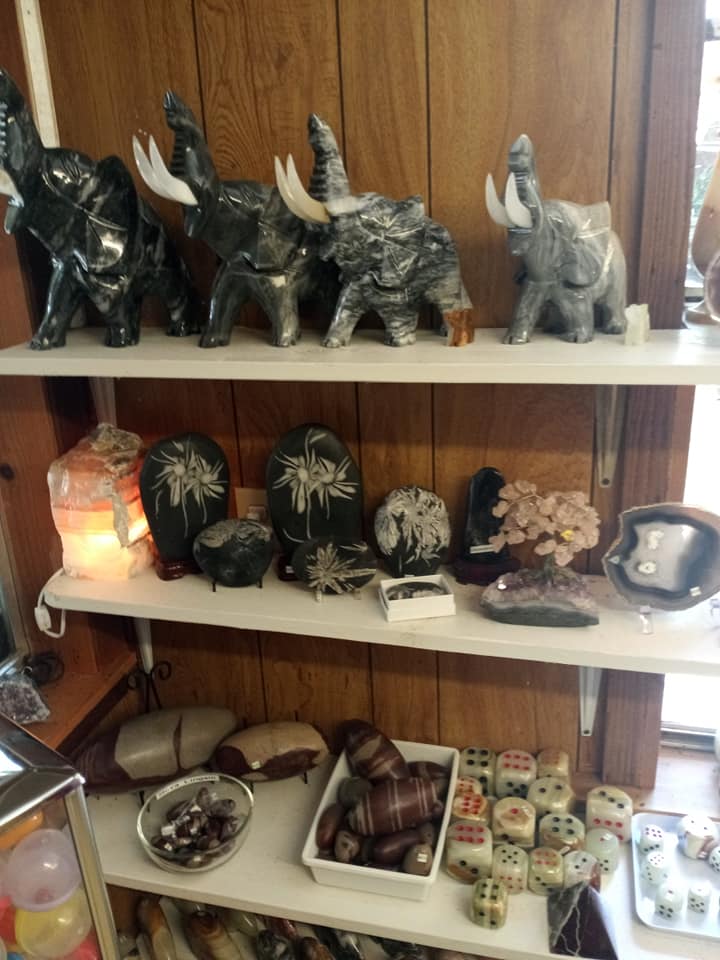 Wooden shelves displaying elephant figurines, crystals, candles, and small decorative items