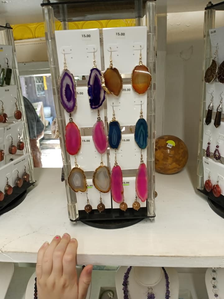 Jewelry display with colorful oval pendants on white stands; hand visible at bottom left.