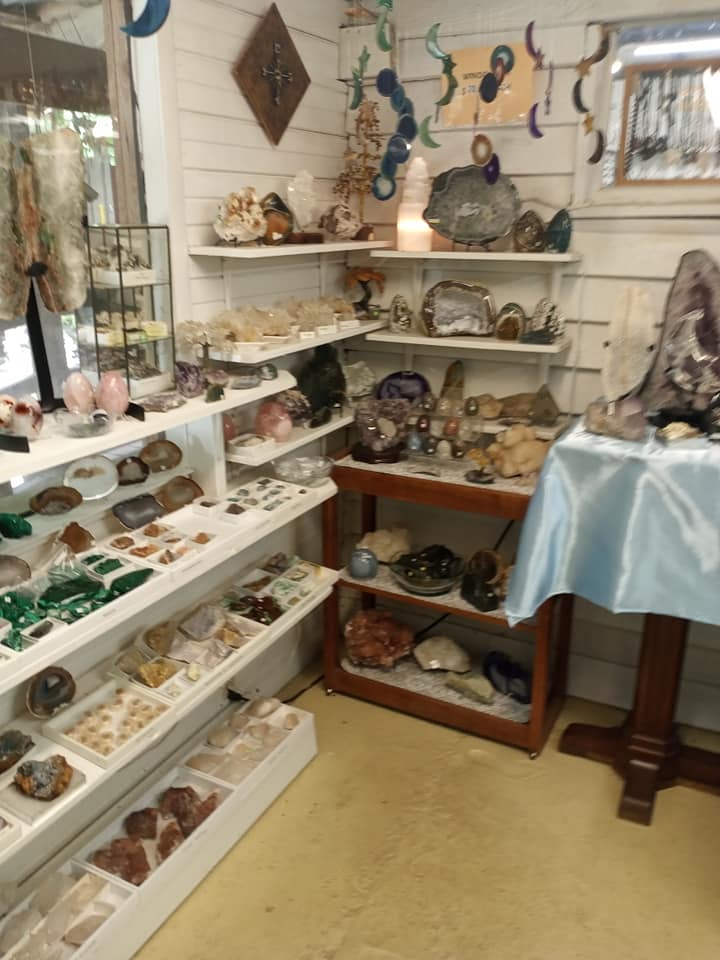 Small crystal and mineral display on white shelves in a shop corner with a blue-draped table.