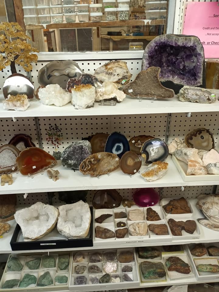 Display shelves of assorted crystals, geodes, and polished stones in a shop, including a large purple amethyst cluster.