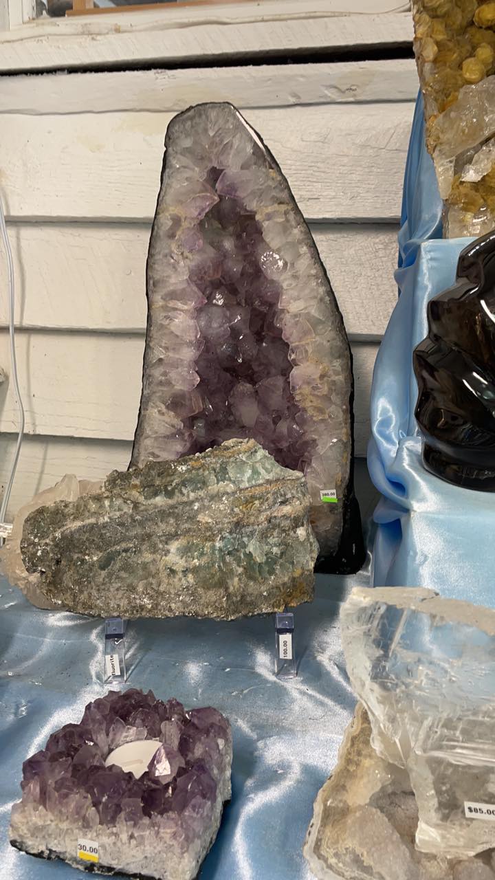 Amethyst crystals and geodes displayed on a blue cloth against a white paneled wall