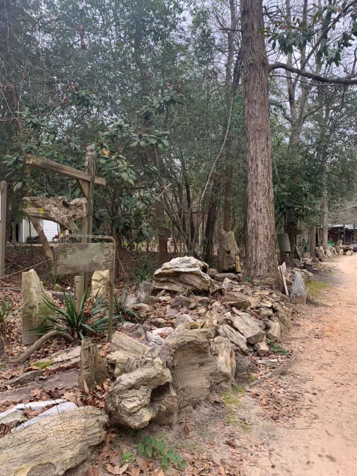Rocky stone wall beside a dirt path in a wooded area with tall trees and a small shelter.