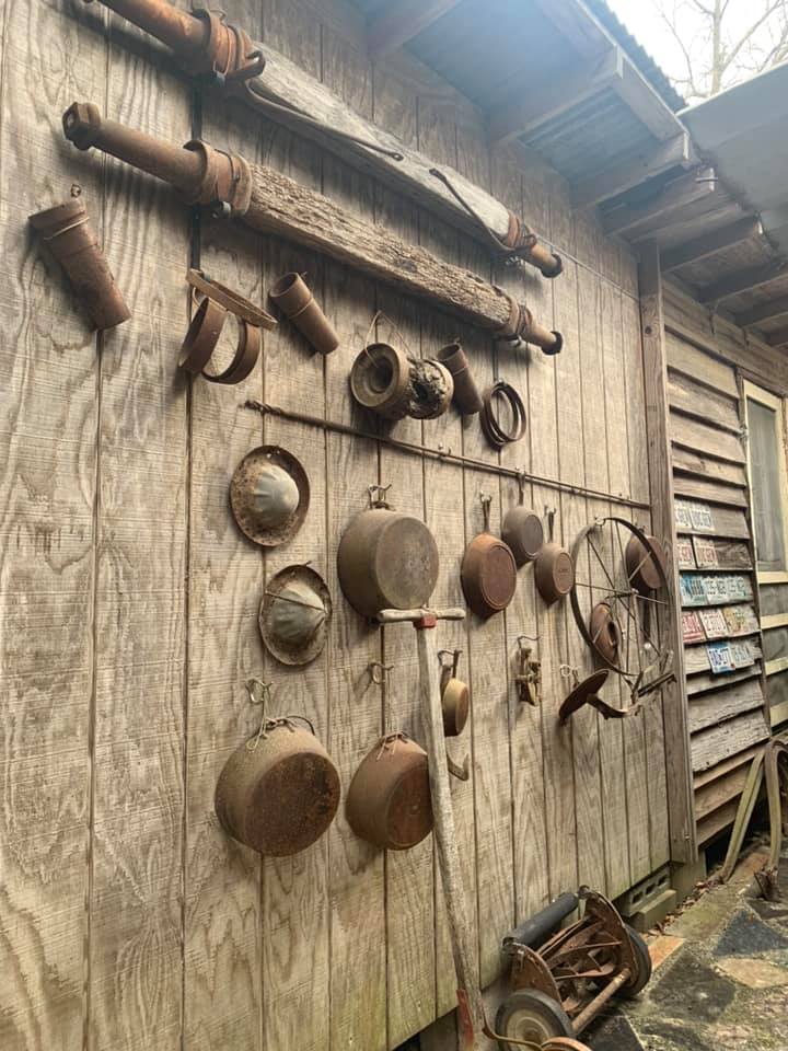 Rustic wooden wall with hanging vintage pans, pots, and tools outside a weathered shed
