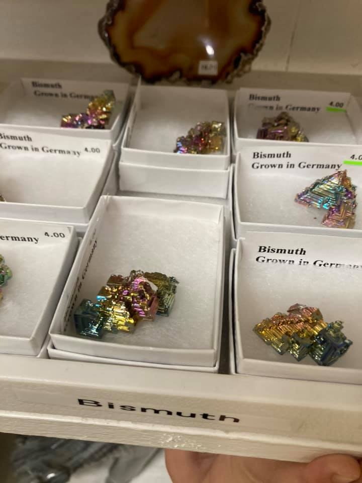 Tray of labeled mineral specimens in white display boxes, with shiny multicolored crystals in several compartments