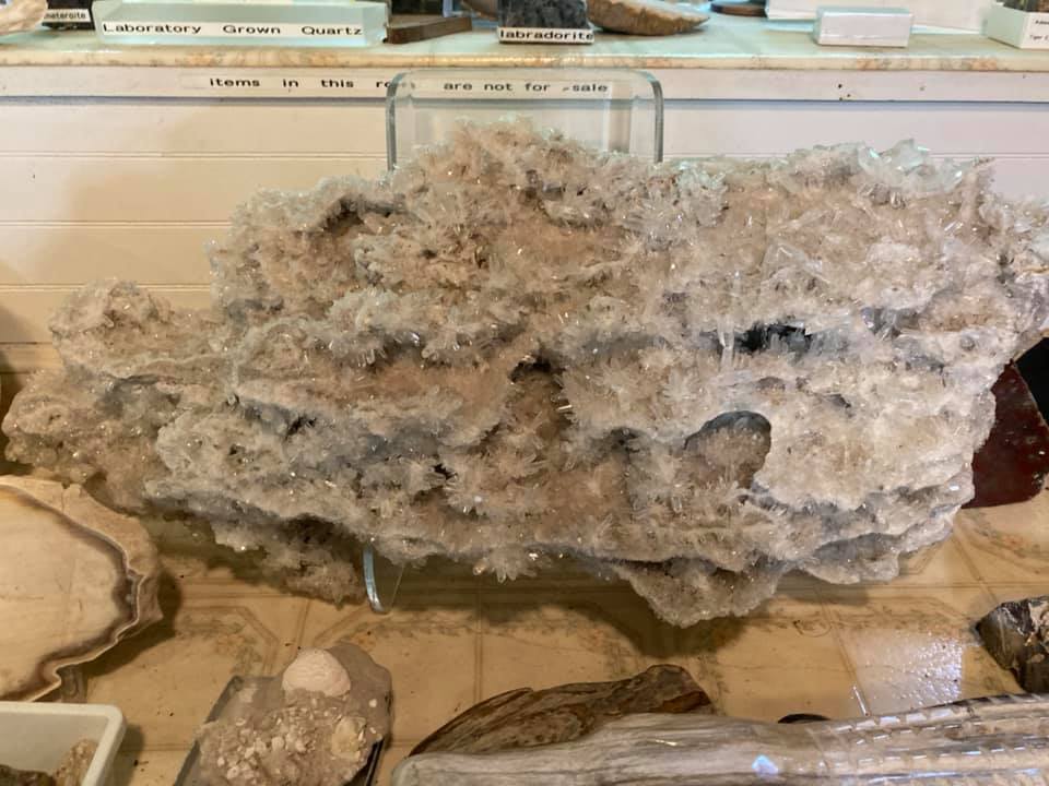 Large rough gray mineral rock displayed in a museum case on a wooden base