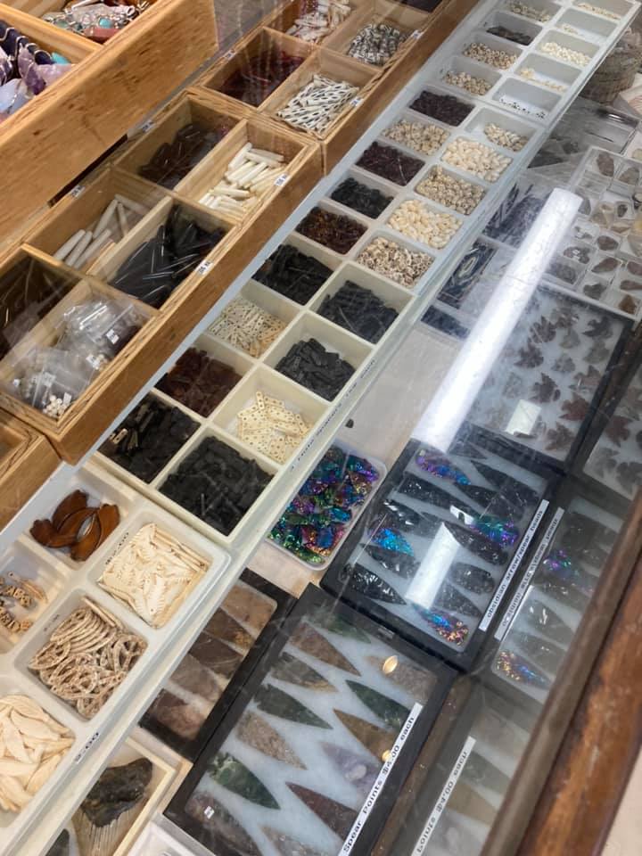 Open display case with assorted small craft supplies and colorful beads in compartment trays