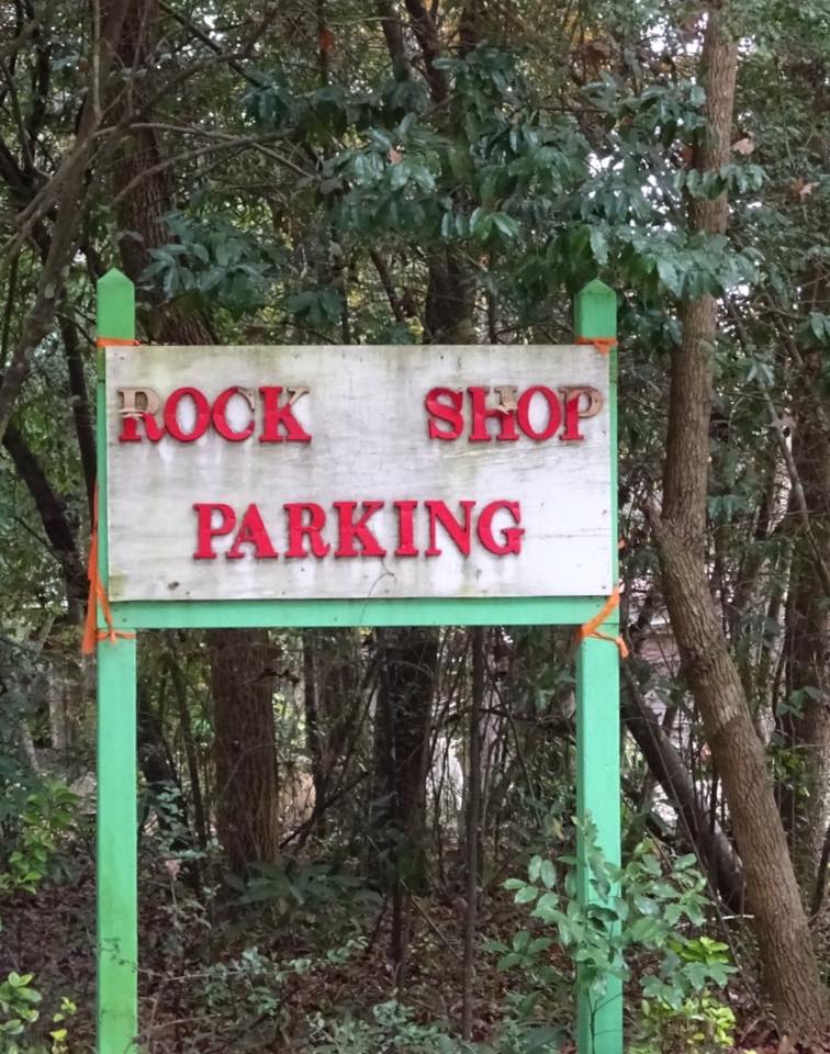 Rock Shop parking sign on a green post in a wooded area.