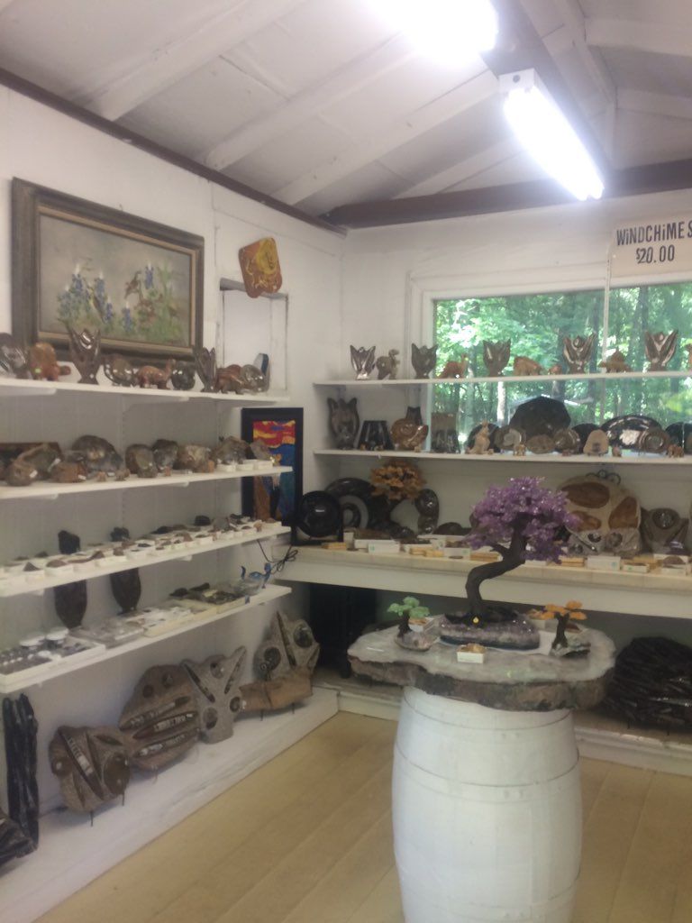 Small shop interior with white shelves of decorative items, a central display table, and a window overlooking greenery