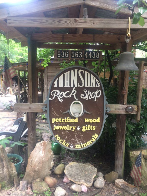 Rustic sign for Johnson’s Rock Shop with petried wood, jewelry, gifts, rocks and minerals under a wooden roof