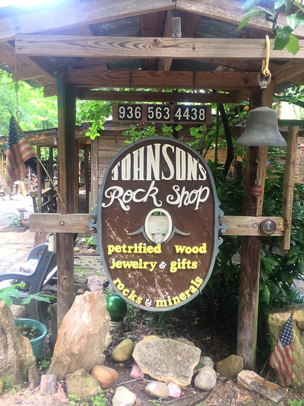 John Sin Rock Shop sign hanging in a rustic wooden outdoor booth with bells and rocks nearby