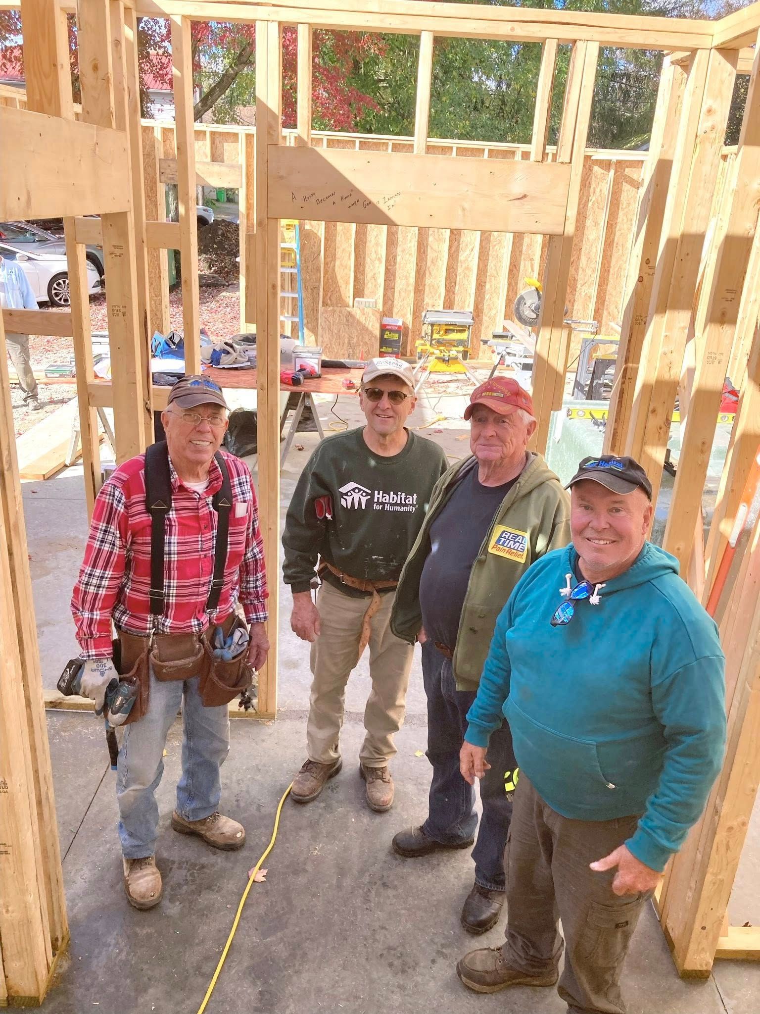 Four construction workers standing inside a framed wooden house under construction.