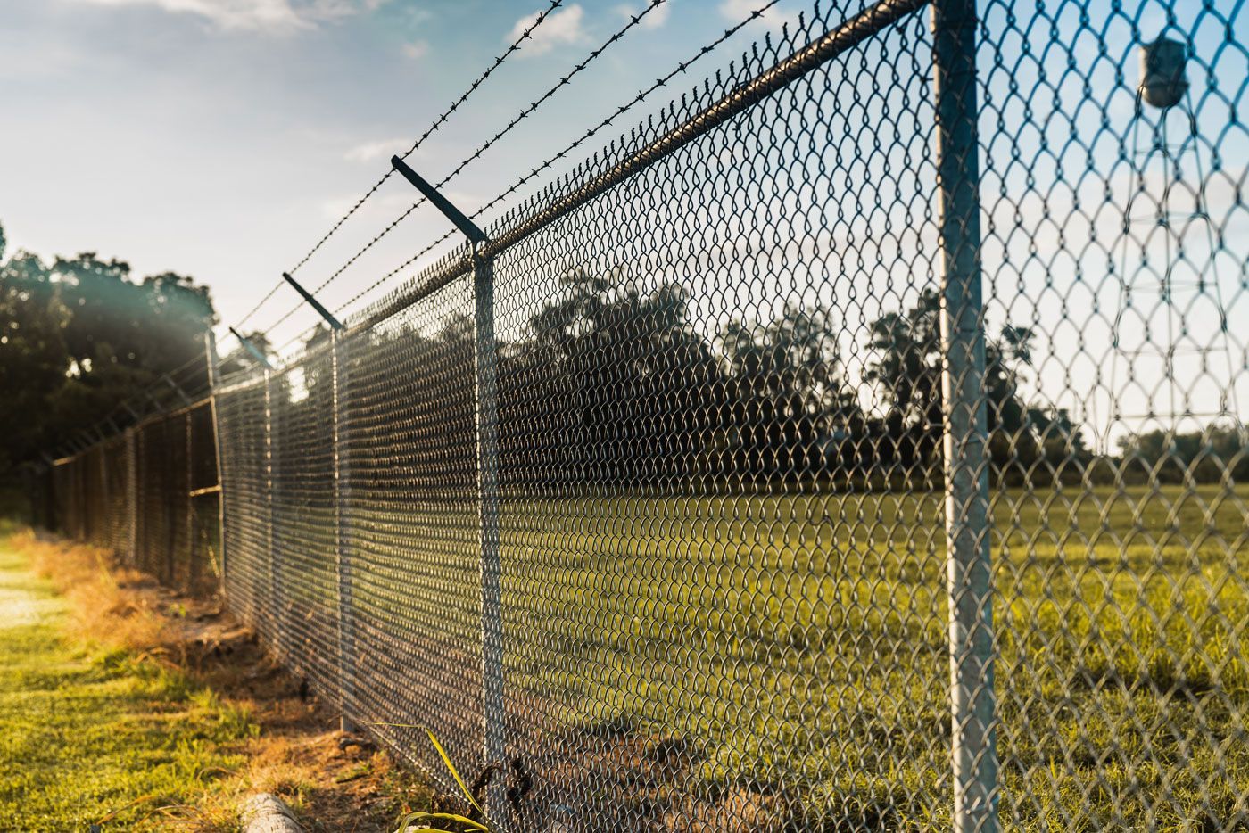 The Power of Versatile Chain Link Fencing A chain link fence with barbed wire surrounding a field.