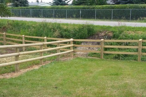 A wooden fence is surrounding a lush green field.