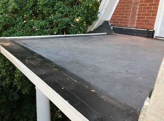 Black flat roof with white trim and a brick chimney in the background.