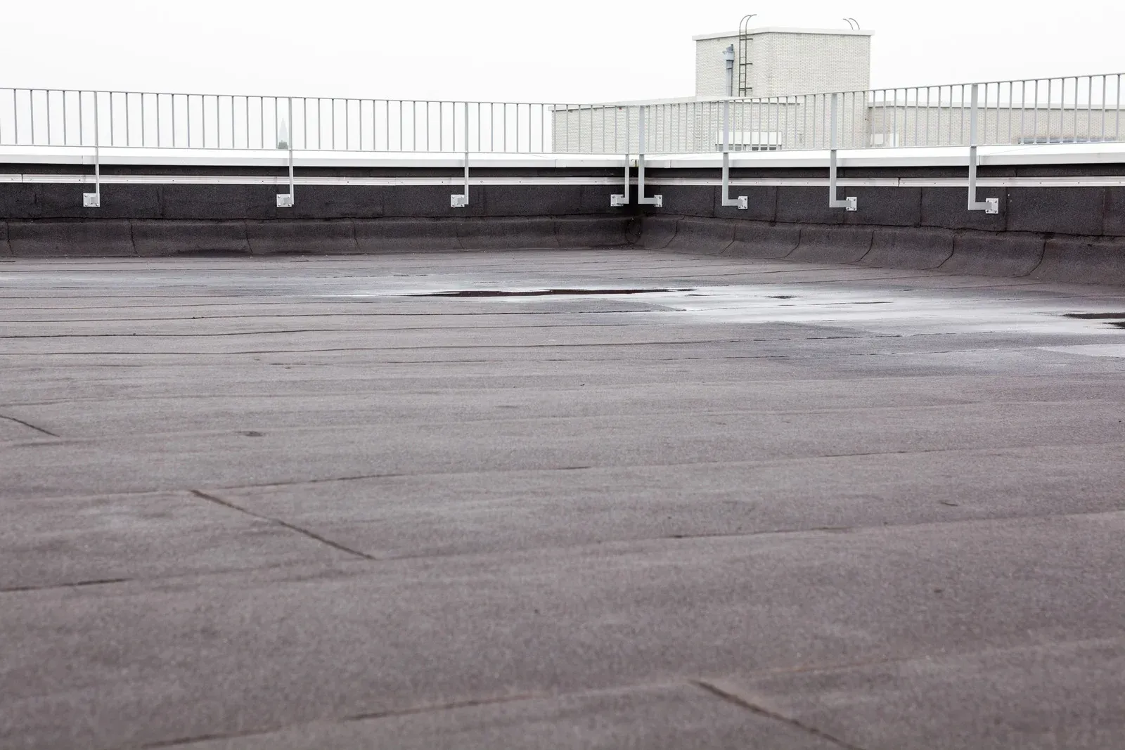 Flat, dark roof with metal railing and brackets; patches of moisture visible.