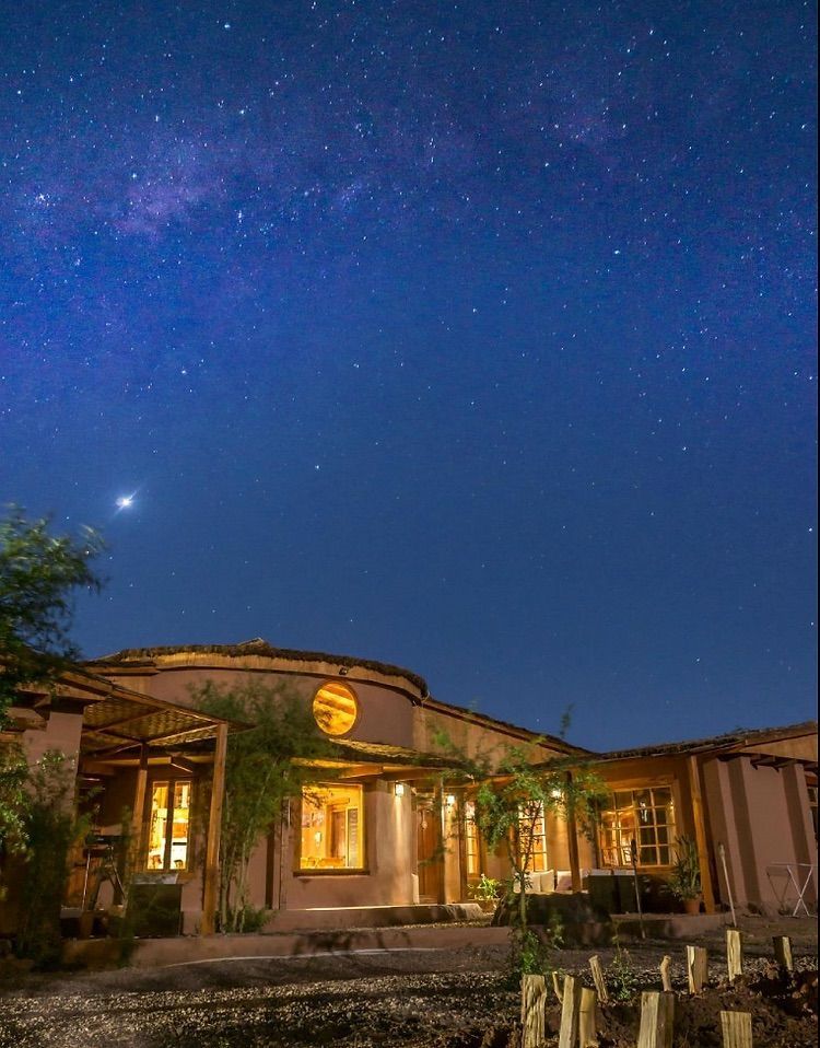 Cabaña en el desierto de noche bajo un cielo estrellado. Edificios iluminados con una cálida luz.