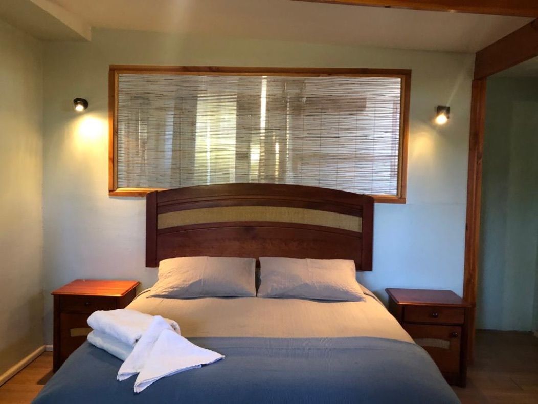 Dormitorio con estructura de cama de madera, dos mesitas de noche y una ventana con persiana de bambú.