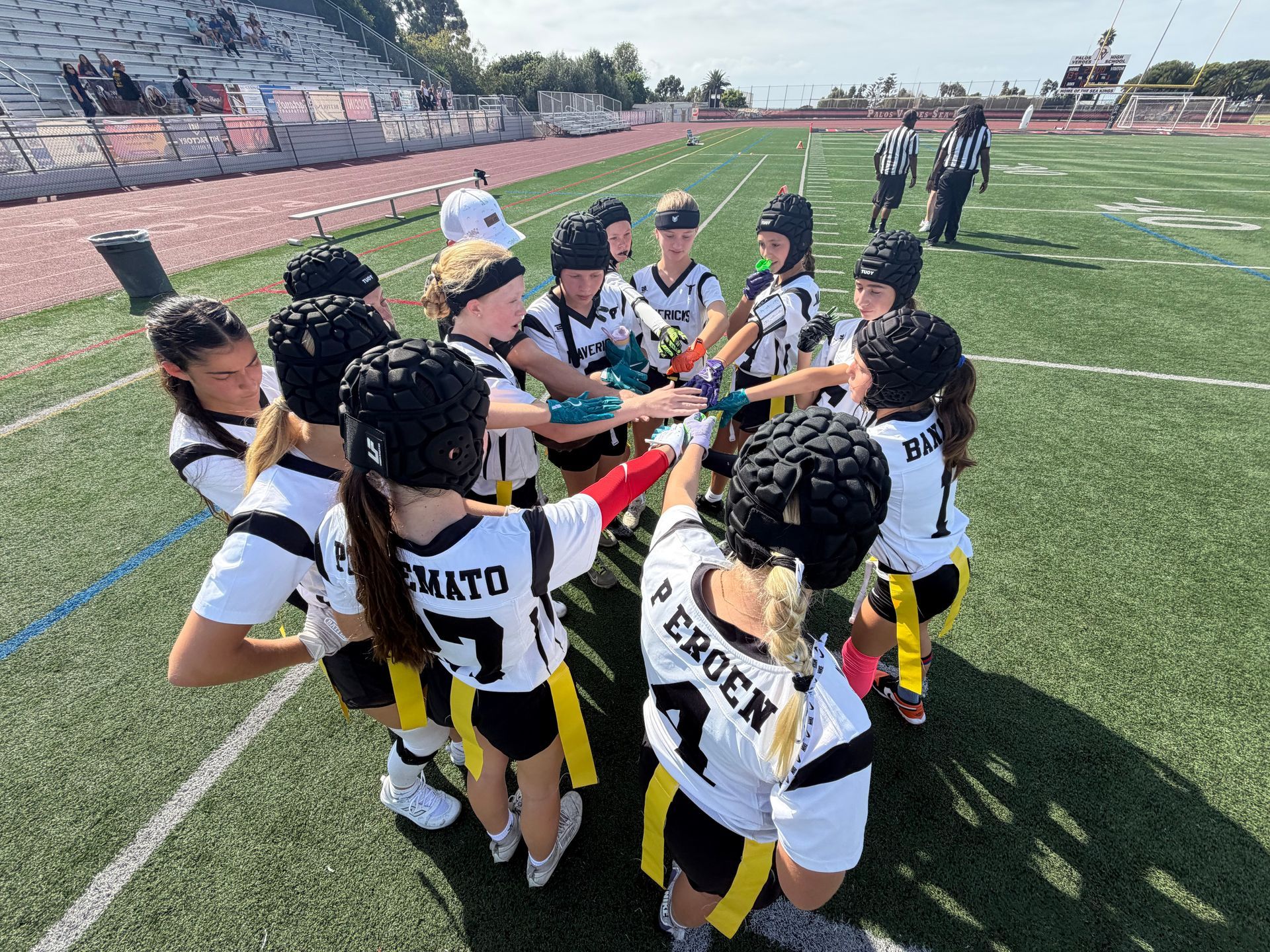 Youth soccer team huddles on a field, stacking hands before a game under sunny skies