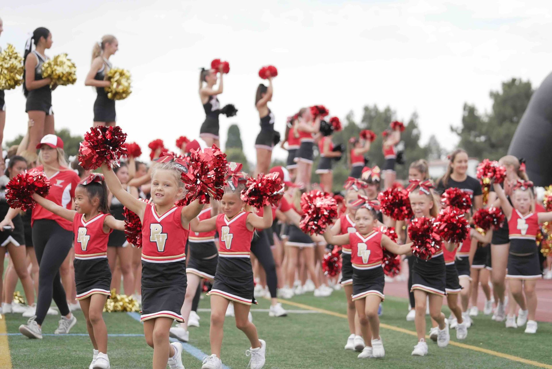 Cheerleaders in red uniforms with pom-poms perform on a football field during a game sideline routine