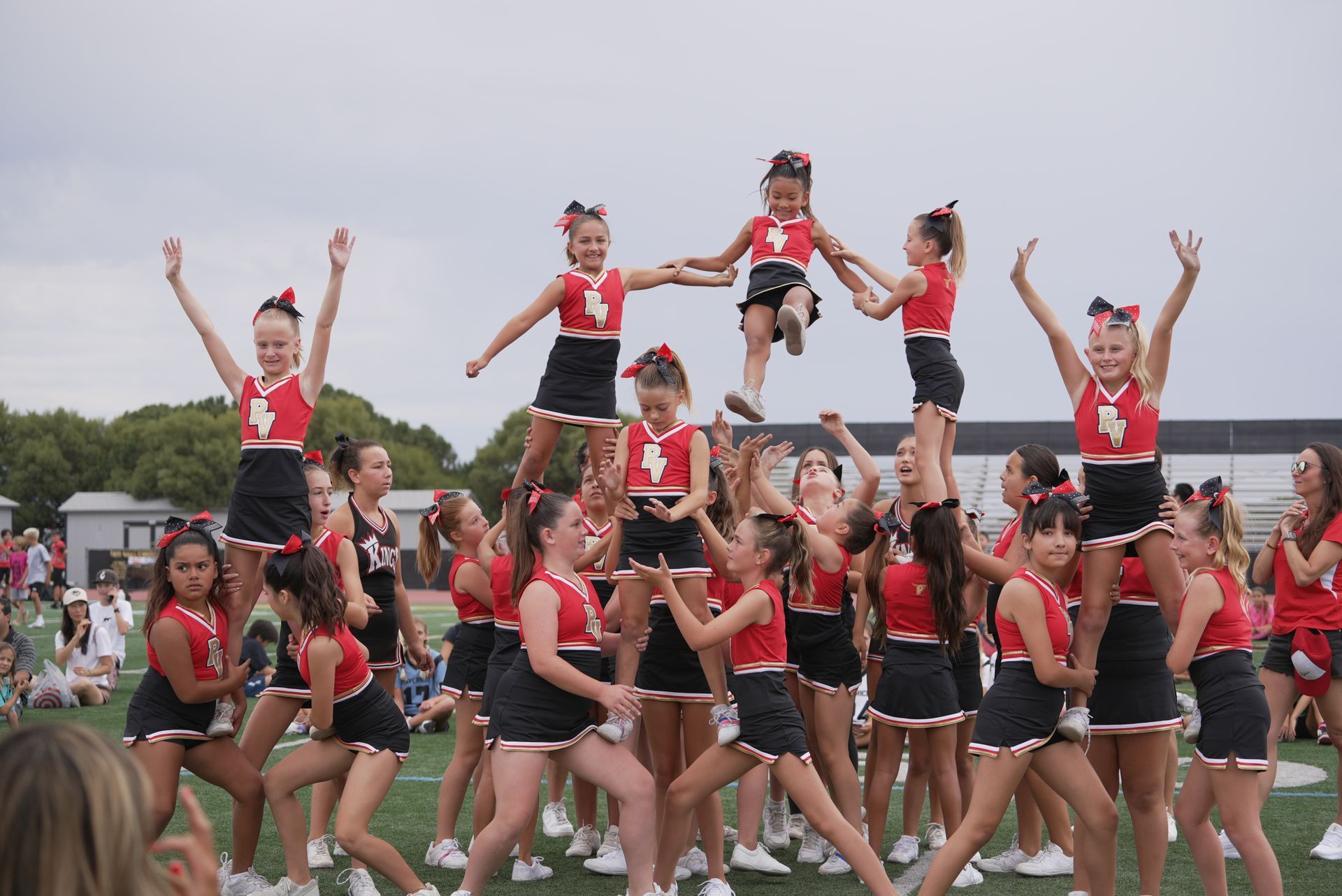 Cheerleading team in red and black uniforms performing a stunt outdoors on a field