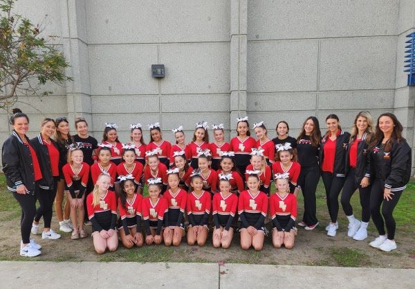 Group of people in red and black outfits posing outdoors in front of a gray wall