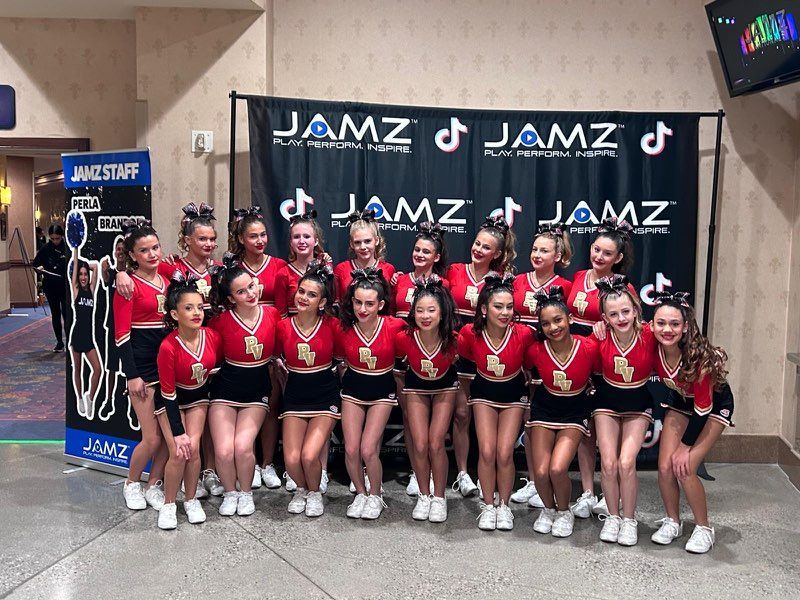 Dance team in red and black uniforms posing at a JAMZ competition backdrop.