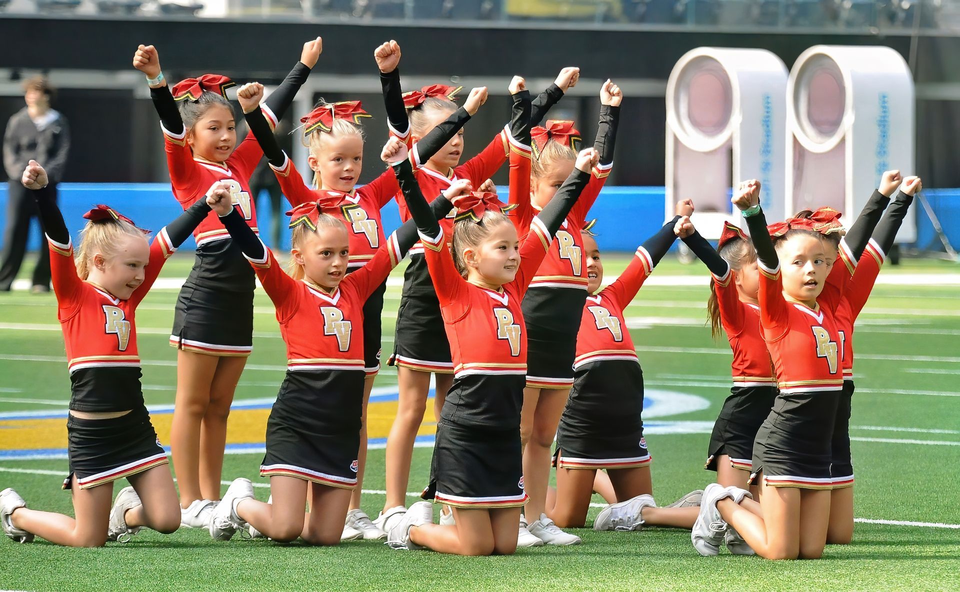 Cheerleading team kneeling on a sports field with arms raised in a synchronized routine
