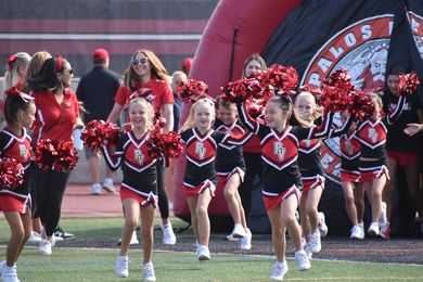 Cheerleader in red uniform performs a backbend on a green and red football field.
