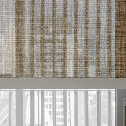 Woven shades partially cover a window, creating a striped shadow pattern. A bright cityscape can be seen through the window.