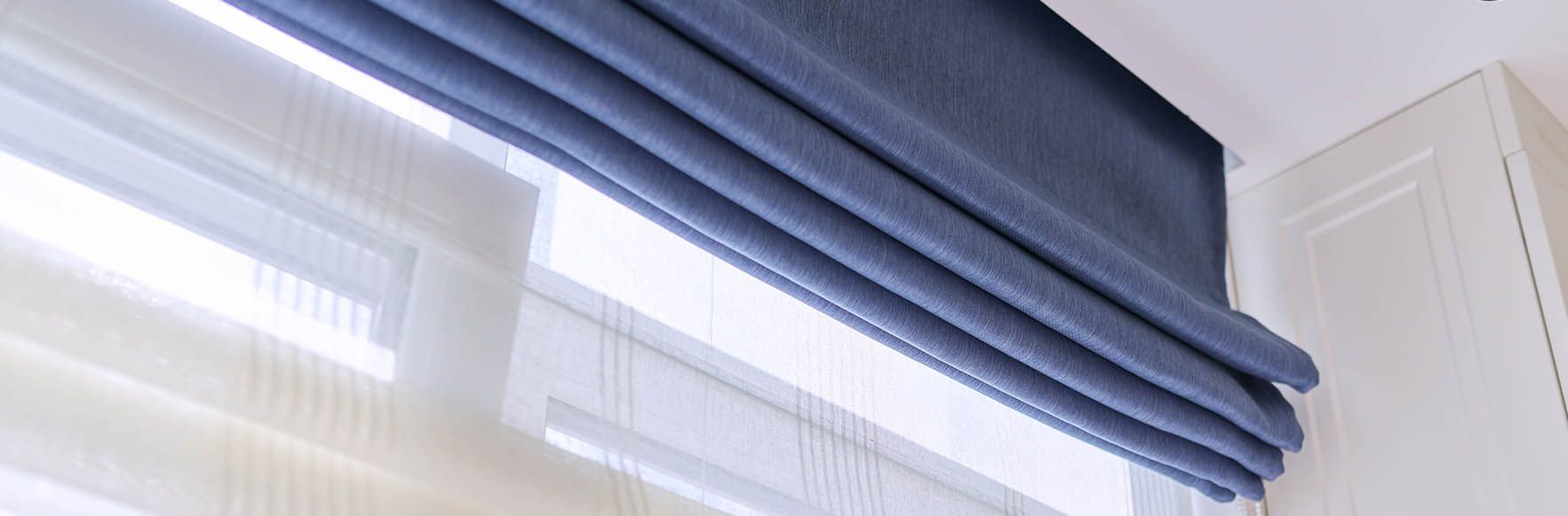 Blue Roman shade partially covering a window. White trim and cabinetry.