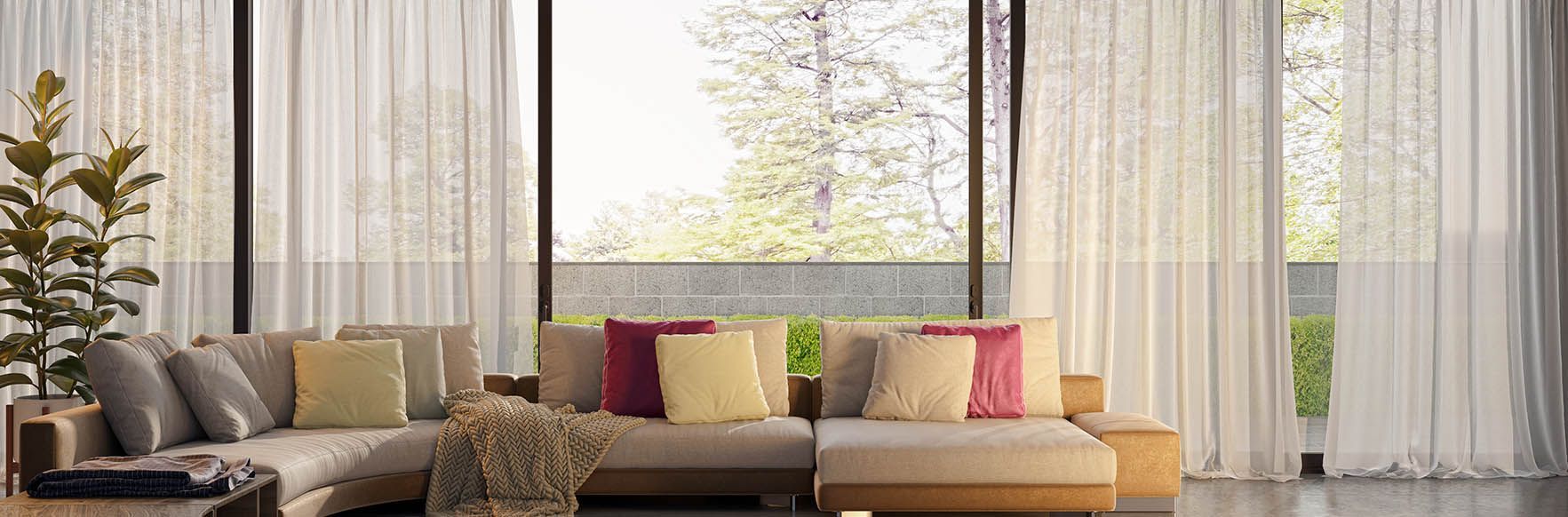 Living room with large windows, sheer curtains, a beige sectional sofa, and colorful throw pillows.