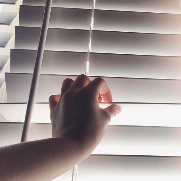 Hand reaching through a partially open window blind, letting in light.