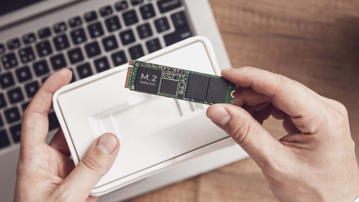 A person is holding a ssd in front of a laptop.