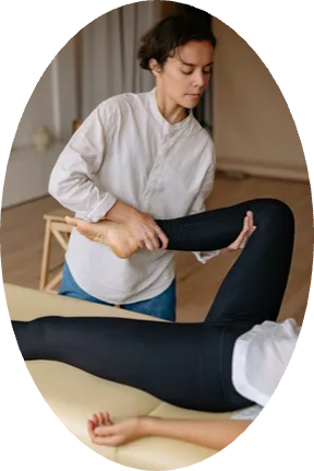 A woman is stretching another woman 's leg on a table.