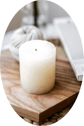 A white candle is sitting on a wooden cutting board next to a laptop.