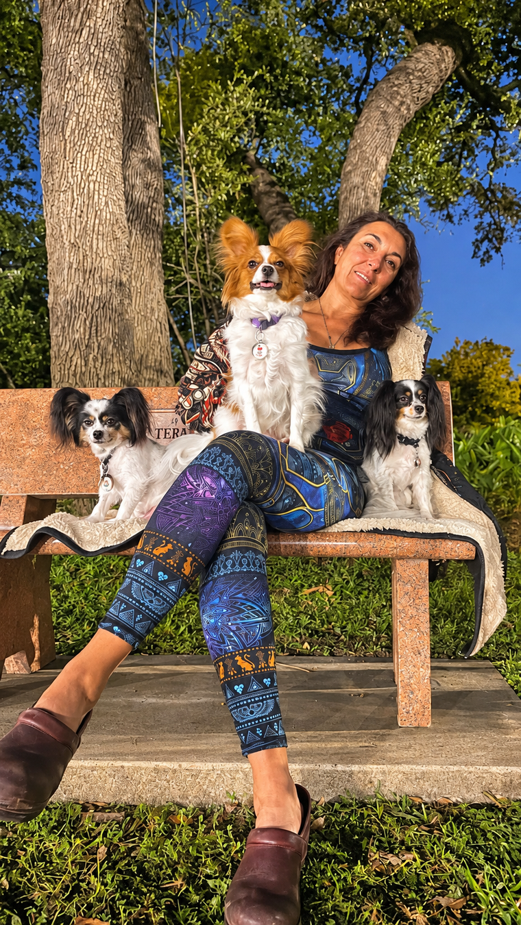 Person in a furry hat holding a small white-and-brown dog in a purple jacket outdoors