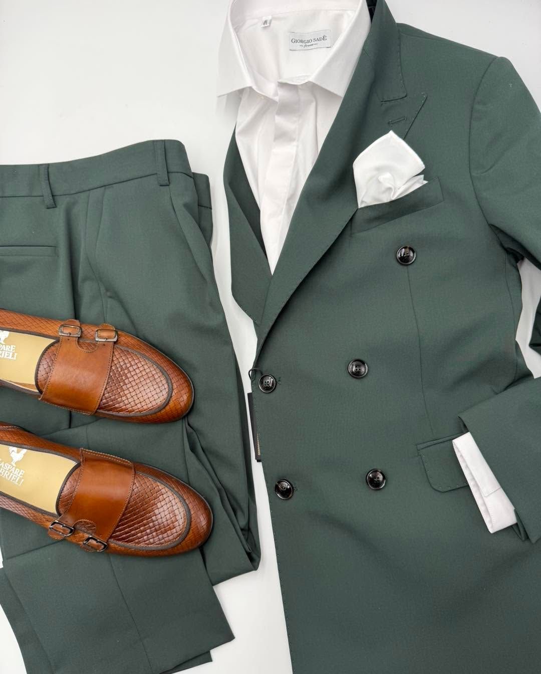 Abito verde con camicia bianca, fazzoletto da taschino e mocassini marroni, disposti su sfondo bianco.