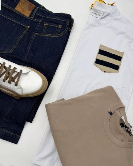 Jeans scuri, camicia bianca con taschino a righe, maglione beige e scarpe da ginnastica bianche su sfondo bianco