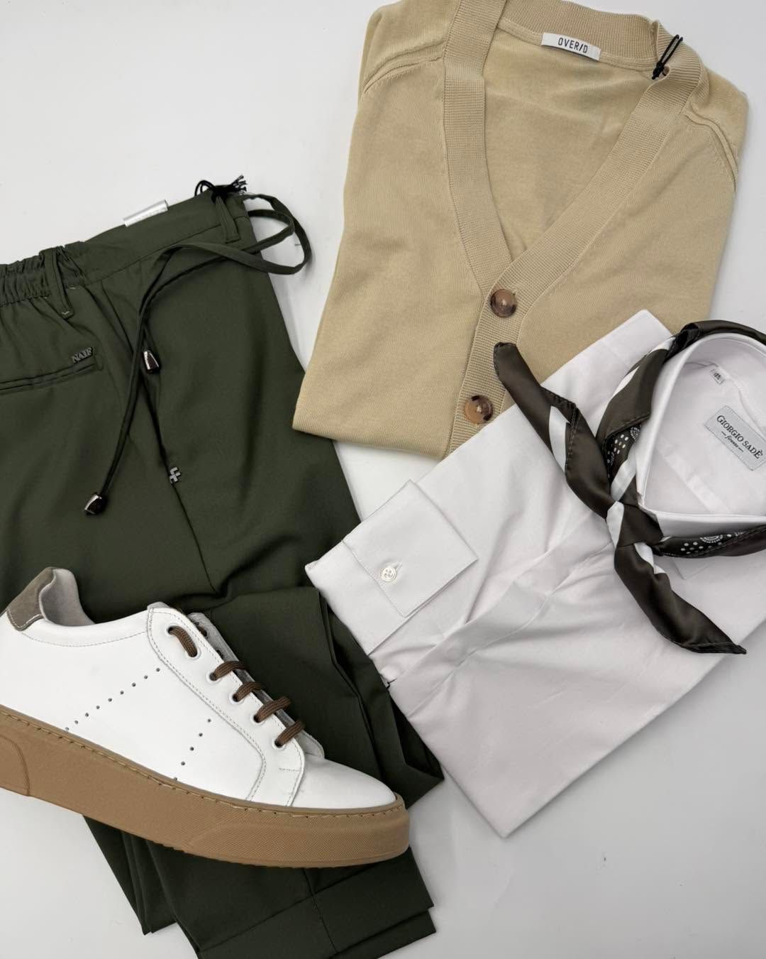 Scarpa da ginnastica bianca con suola beige accanto a pantaloni verde oliva, pantaloncini color cachi e camicia bianca con sciarpa su sfondo bianco