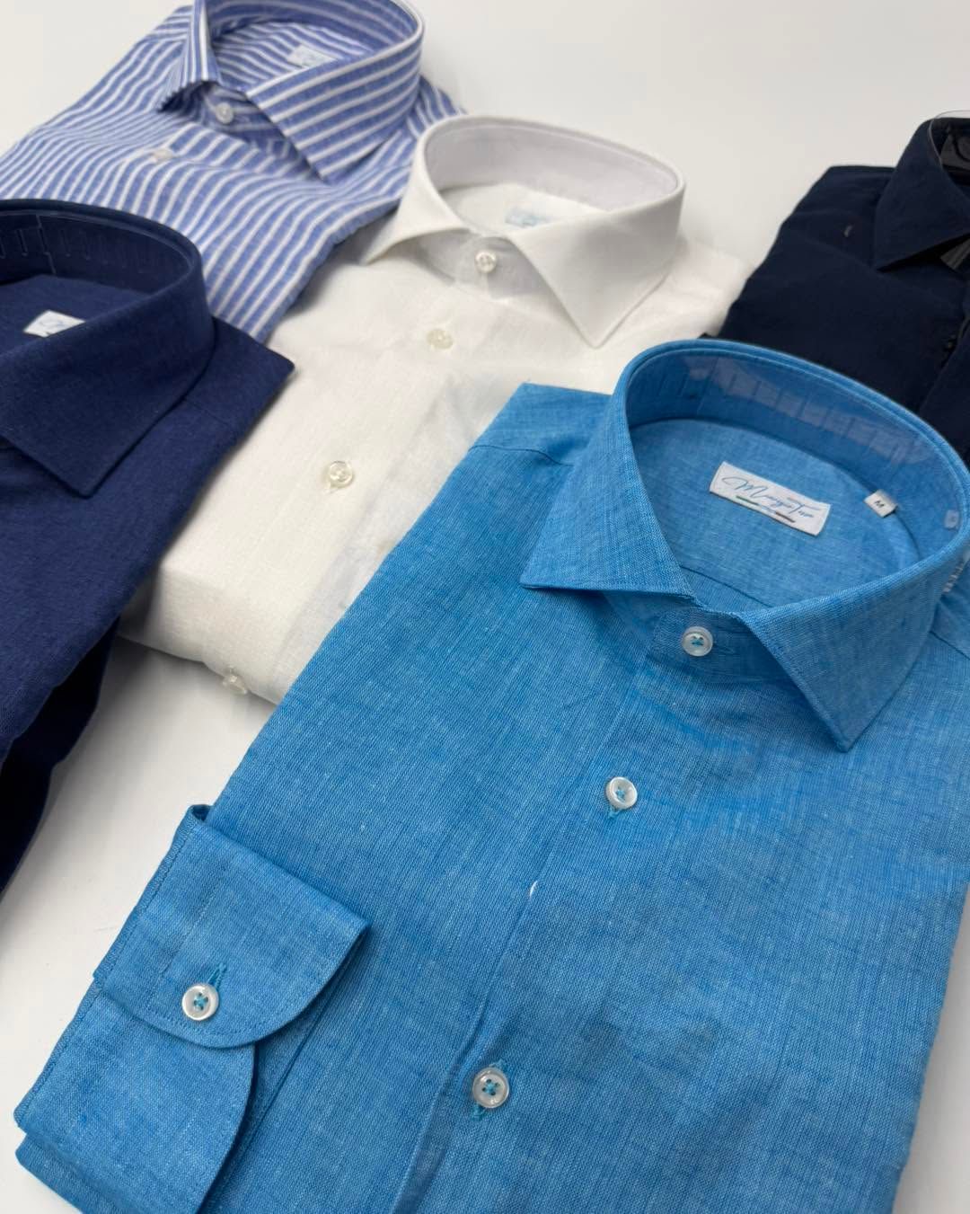 Diverse camicie eleganti piegate, nei toni del blu, del bianco e del blu scuro, disposte insieme.