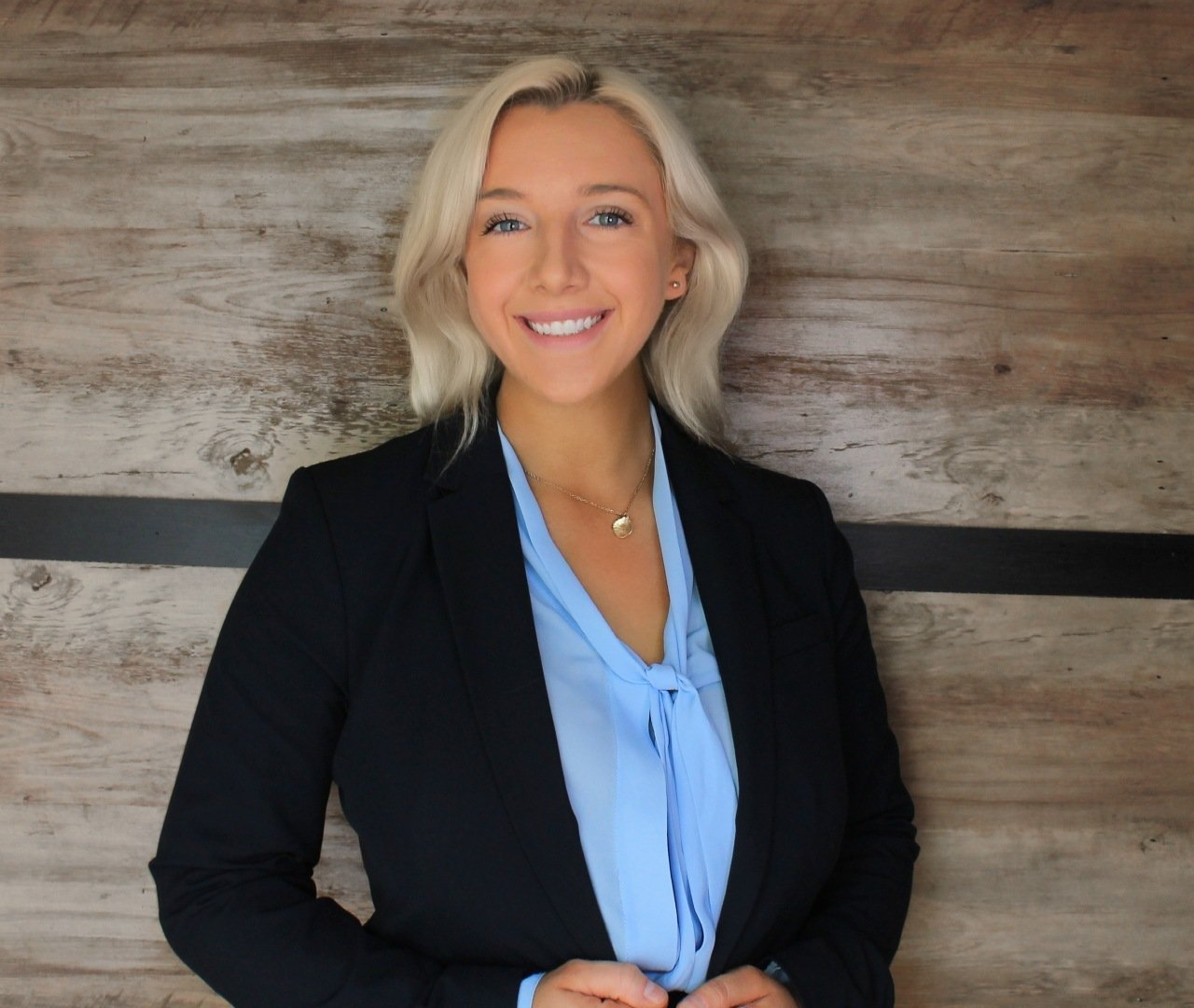 A woman in a blue shirt and black jacket is smiling