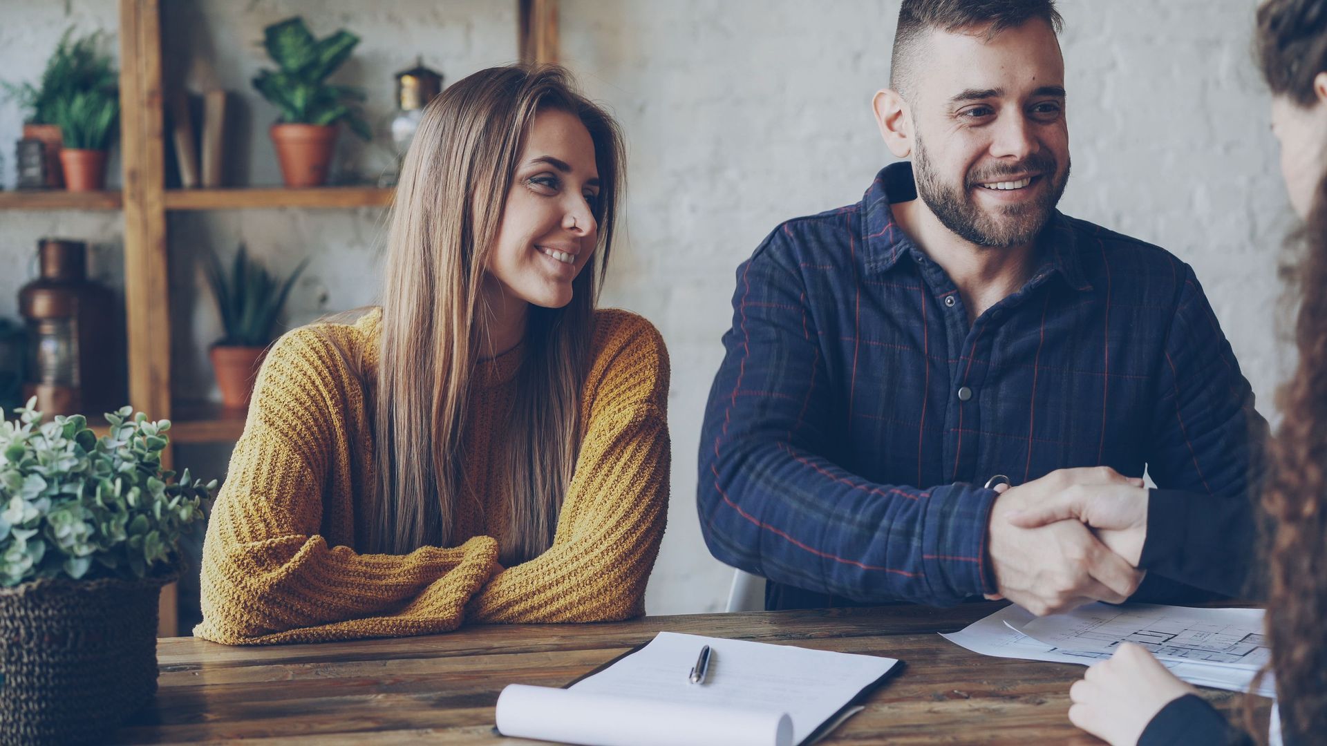 Two coworkers smiling at a table with a notebook in a cozy office setting