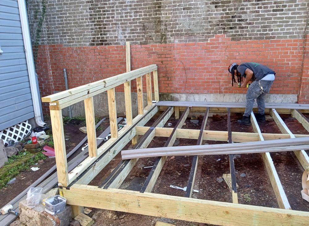 A man is working on a wooden deck in front of a brick wall.
