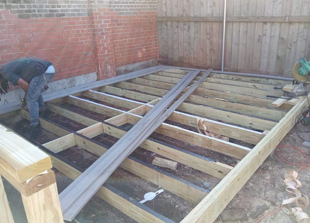 A man is working on a wooden deck in a backyard.