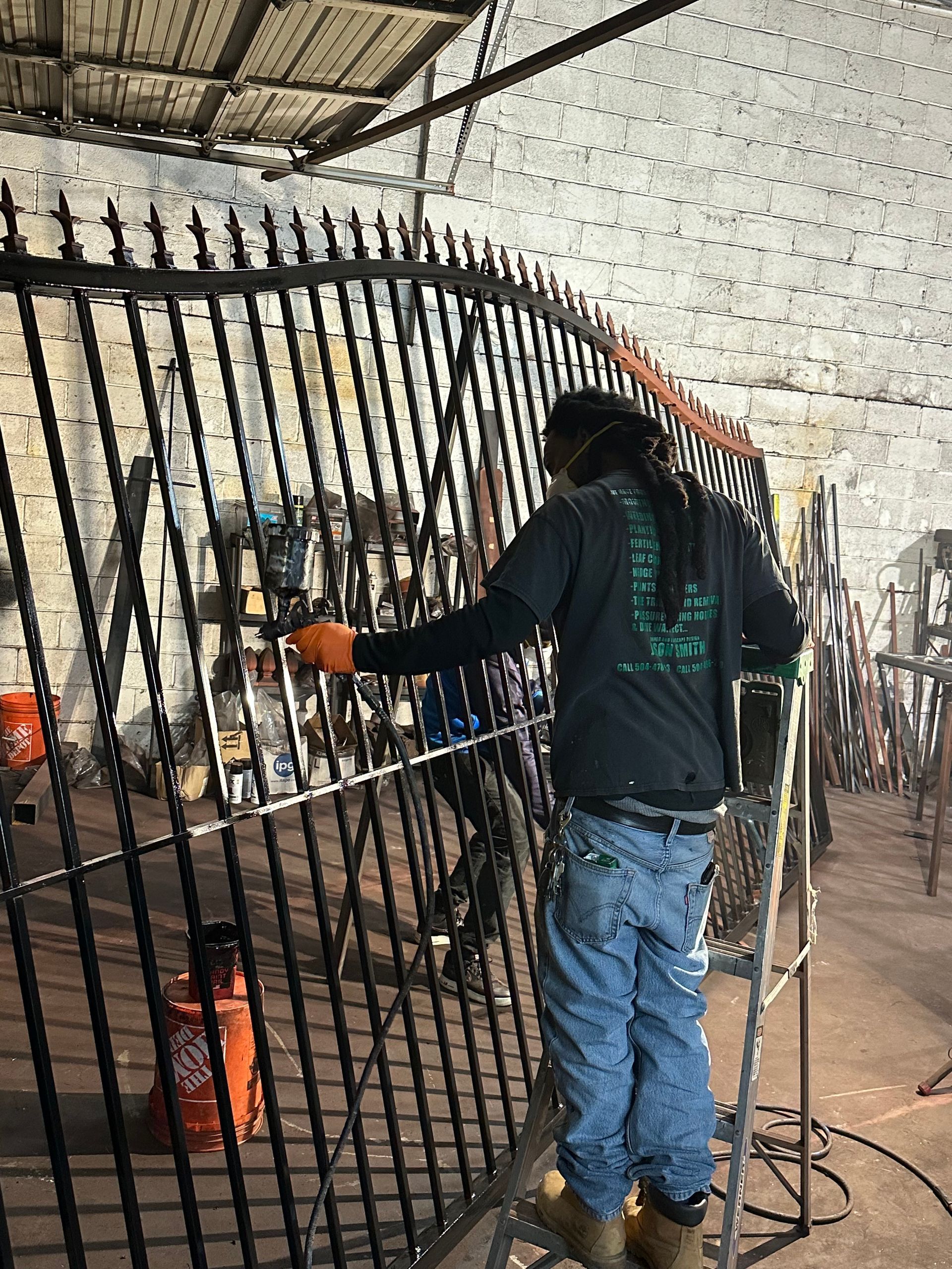 A man is standing on a ladder working on a metal fence.