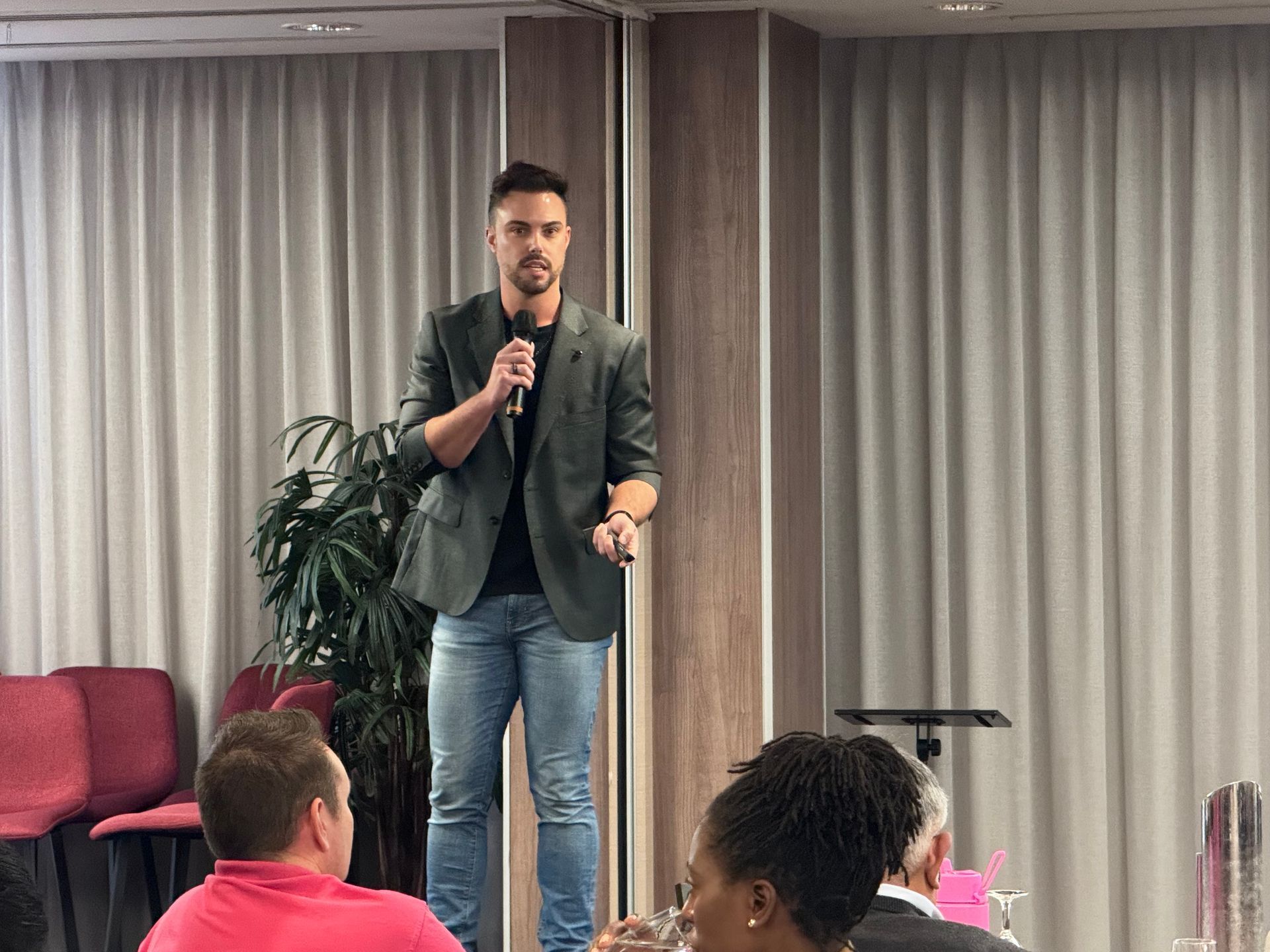 Man in blazer speaks into microphone at event.