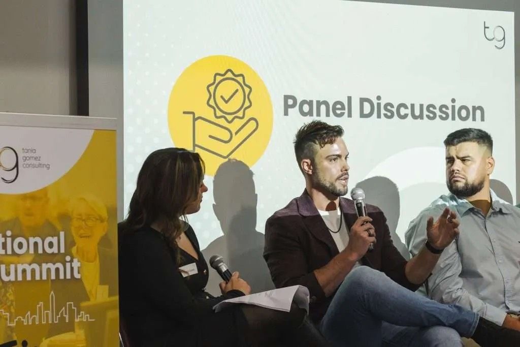 Panel discussion with three speakers at a conference. The panel banner is yellow.