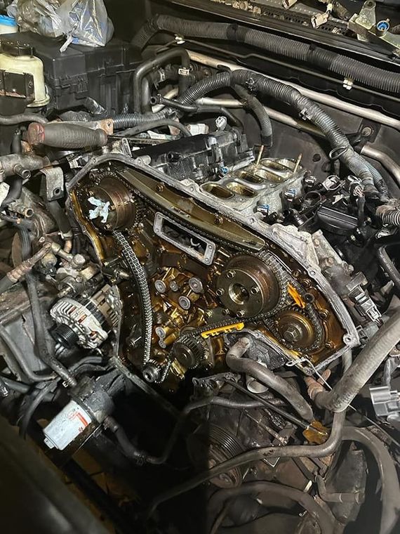 An exposed car engine with timing chains, sprockets, and internal metal components visible inside the engine bay.