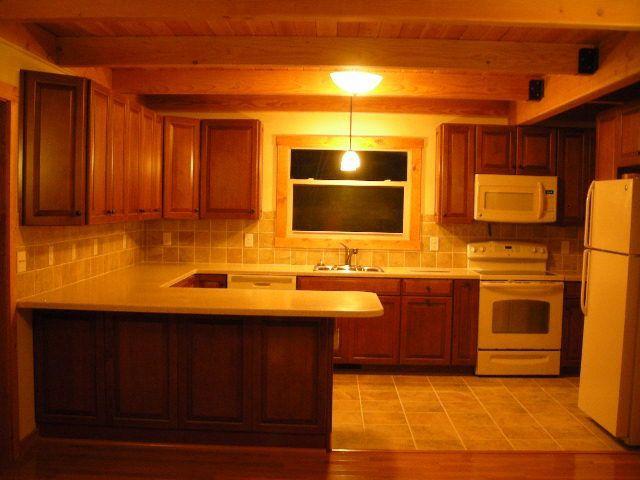 Kitchen with wooden cabinets, beige countertops, and appliances like a stove, microwave, and refrigerator.